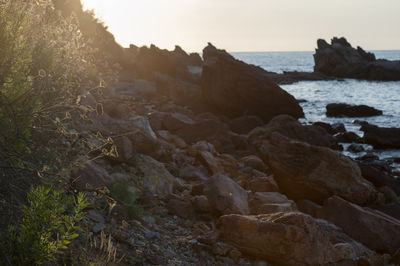 Rocks on beach against sky during sunset