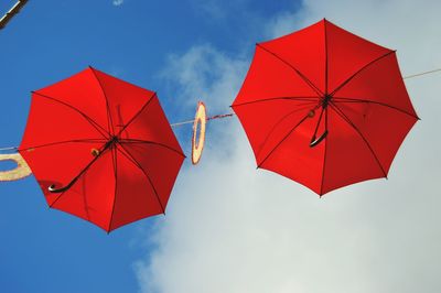 Low angle view of red umbrellas hanging against cloudy sky