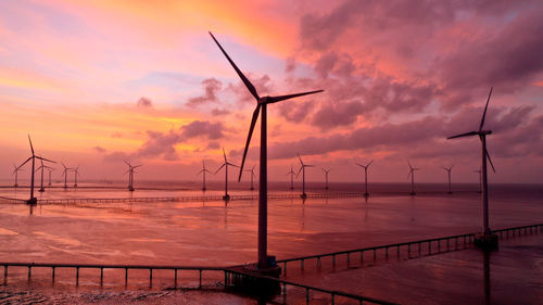 Wind turbines on land against sky during sunset