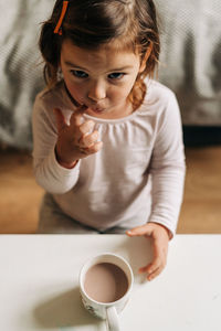 High angle portrait of cute girl standing by hot chocolate at home