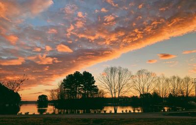 Silhouette trees by lake against sky during sunset