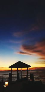 Silhouette built structure on beach against sky during sunset