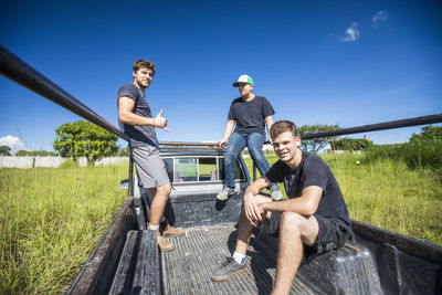 Three young men ride through field in back of 4x4 truck.