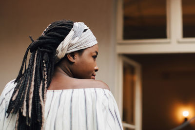 Rear view of young woman looking away while standing against house