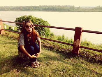 Portrait of woman in sunglasses sitting at lakeshore