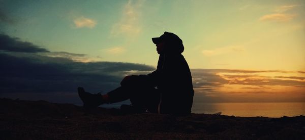 Silhouette person sitting on land against sky during sunset