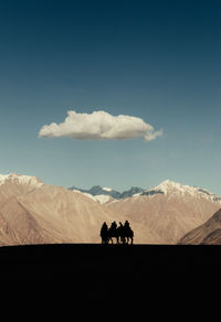 People riding camels in a valley against sky