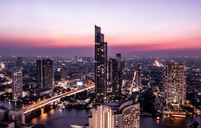 Illuminated buildings in city against sky at sunset