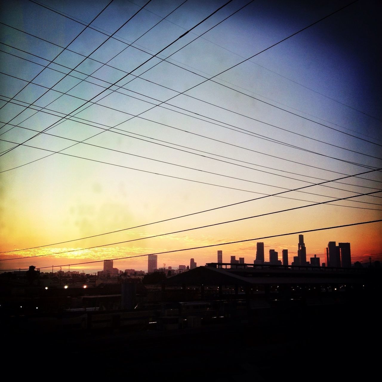 sunset, silhouette, architecture, building exterior, built structure, sky, city, power line, orange color, connection, dusk, cloud - sky, electricity pylon, cityscape, building, low angle view, cloud, dark, cable, urban skyline