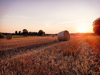 Hay bales on field against sky during sunset