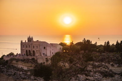 Buildings by sea against sky during sunset