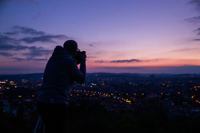 Man photographing cityscape against sky during sunset