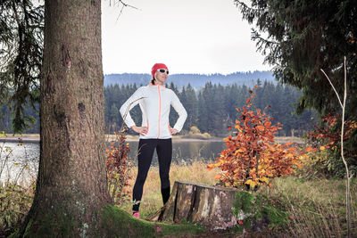 Full length of mature woman with arms akimbo standing against trees in forest