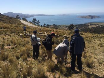 Rear view of people on field photographing lake