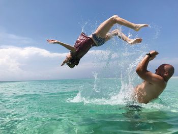 Side view of girl jumping from shirtless father in sea against sky