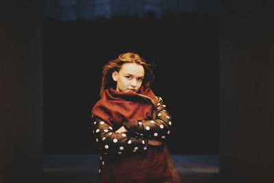 Portrait of young woman standing against black background