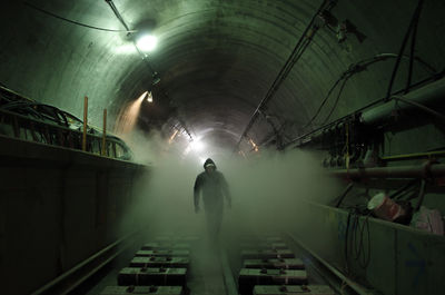 Man walking amidst smoke on railroad track in illuminated subway tunnel