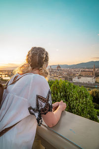 Rear view of woman with umbrella standing against sky during sunset