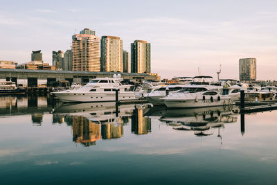 Boats moored at harbor against sky in city