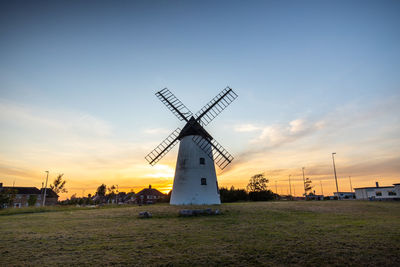 Traditional windmill on field against sky during sunset