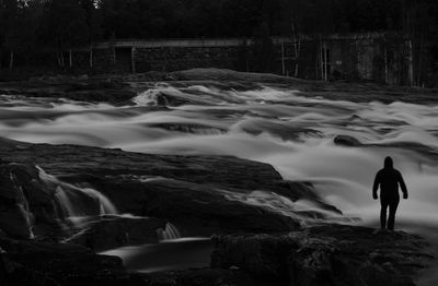 Man standing on rocks by waterfall