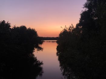 Silhouette trees by lake against sky during sunset