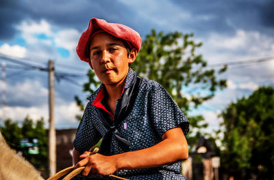 Portrait of boy sitting on horse against sky