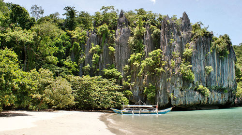 Outrigger canoe moored on shore by rocky mountain