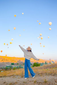 Rear view of woman with arms outstretched standing on field against sky