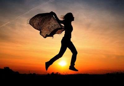 Silhouette woman jumping against orange sky