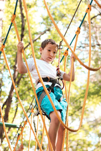 Low angle view of boy on obstacle course in forest