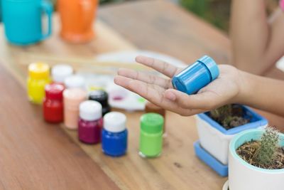 Cropped hand of person holding watercolor paints bottle on table