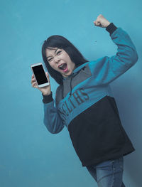 Smiling young woman using phone while standing against blue sky