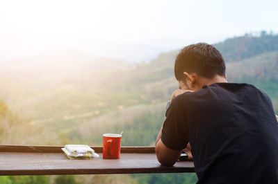 Rear view of man sitting at table against mountains