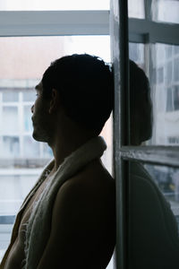 Portrait of young man looking through window at home