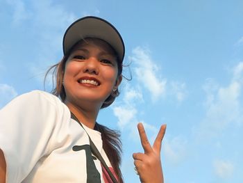 Low angle portrait of woman showing peace sign against sky