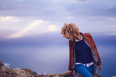 Woman sitting on rock against sky