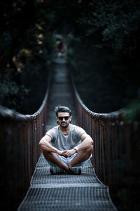 Portrait of man in sunglasses sitting on footbridge