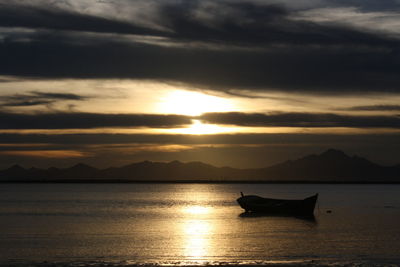 Silhouette man in boat on sea against sunset sky