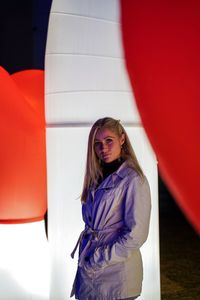 Portrait of young woman standing against column at night