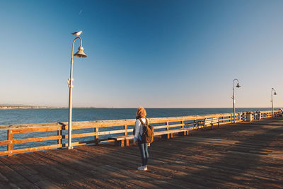 Rear view of woman standing at beach against clear sky