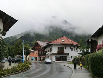 Houses on road amidst buildings against sky during rainy season