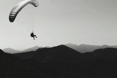 Person paragliding over mountain against sky