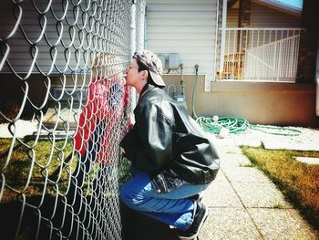 Side view of mother kissing son through chainlink fence