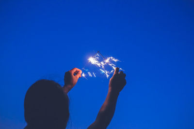 Low angle view of woman holding hands against blue sky