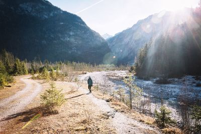 Rear view of woman walking on pathway amidst mountains during sunny day