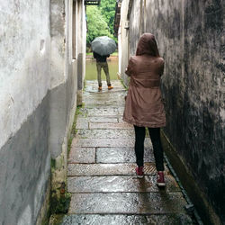 Rear view of man and woman standing on alley amidst houses during rainy season