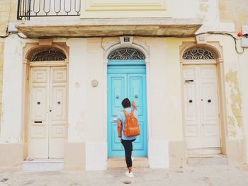 Rear view of man with backpack standing by closed door outside house