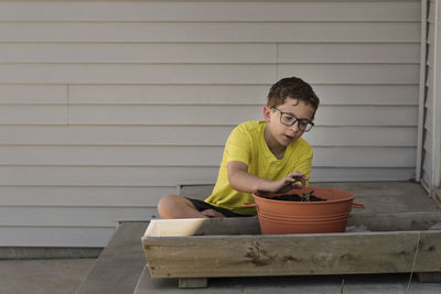 Boy planting sapling in flower pot at backyard