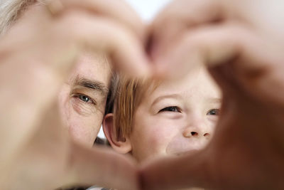 Grandfather and grandson making a heart shape hand gesture together, looking at camera. happy old